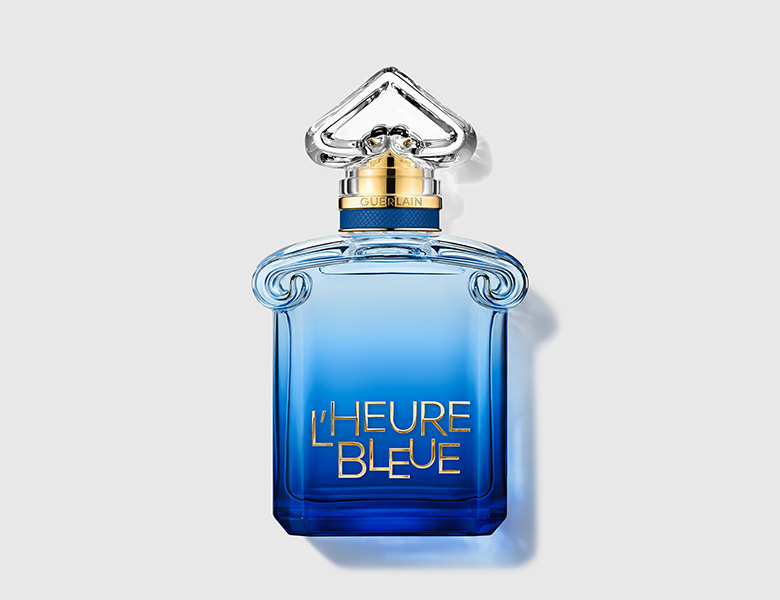 Her ses Guerlain L’Heure Bleue i en blå parfumeflakon med transparent låg og guldfarvede detaljer. På forsiden står teksten “L’Heure Bleue”, og flakonen er placeret mod en lys baggrund.