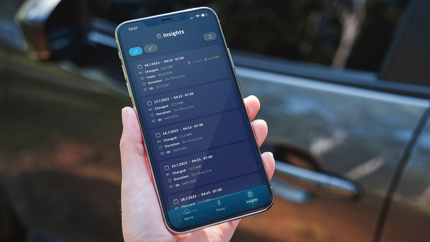 Close-up van een hand die een smartphone vasthoudt met de Eve Connect-app, die een lijst met vermeldingen, tijdvakken en selectievakjes op een blauw scherm toont. Een autodeur is vaag op de achtergrond te zien.