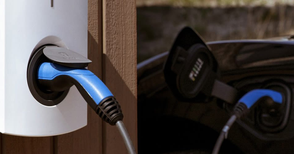 Een elektrische auto wordt opgeladen bij een wandgemonteerd laadstation van Alfen, een blauwe kabel is verbonden met een strakke zwarte auto. De scène laat moderne, milieuvriendelijke technologie zien.