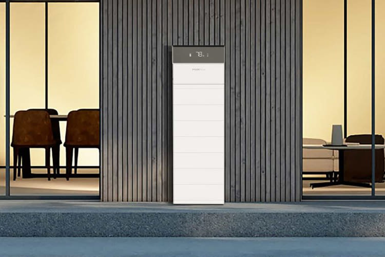 Buiten aanzicht van de entree van een moderne woning met een strak ontwerp en een Pylontech Force H3 thuisbatterij centraal in beeld. Twee auto’s staan geparkeerd op de oprit en van binnenuit straalt warm licht naar buiten.