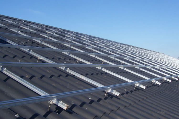 Een dak met rijen zilveren montagematerialen op zwarte dakpannen, klaar voor zonnepanelen, onder een helderblauwe lucht, wat een gevoel van schone energie uitstraalt.