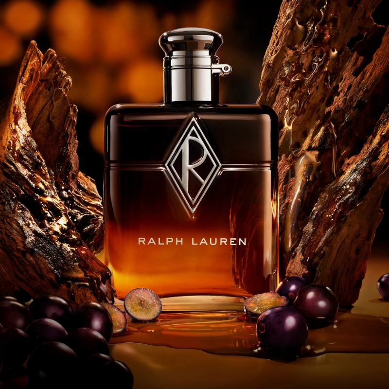 Ralph Lauren-parfymeflaske omgitt av mørke druer og treverk i varmt lys.