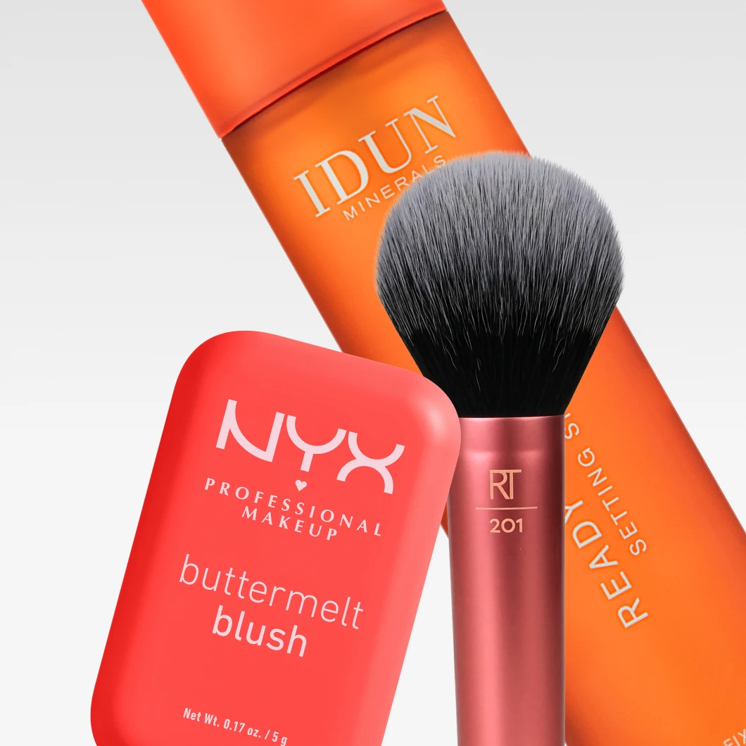 Vaaleanharmaata taustaa vasten esillä ovat IDUN Minerals Ready Set Fix Setting Spray, NYX Professional Makeup Buttermelt Blush ja Real Techniques 201 -meikkisivellin.