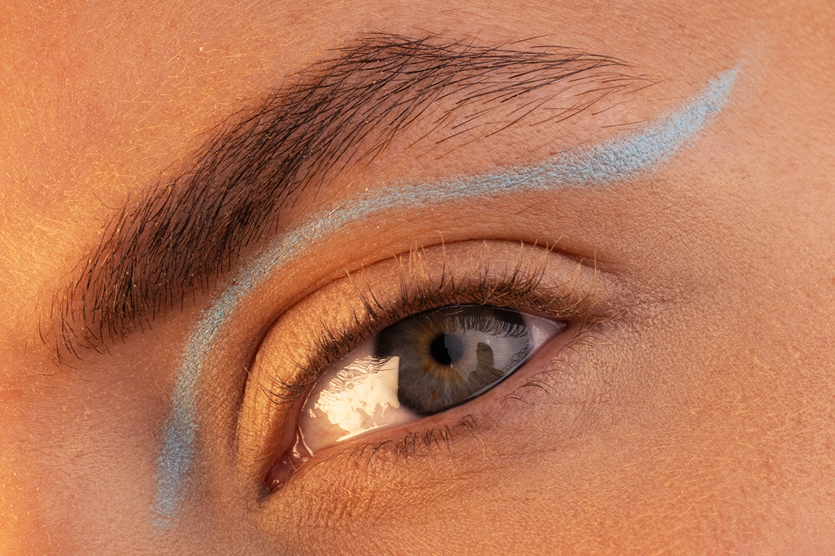 Lähikuva silmästä, jossa on luova sininen eyeliner, joka kulkee luomen ja kulmakarvan yläpuolella
