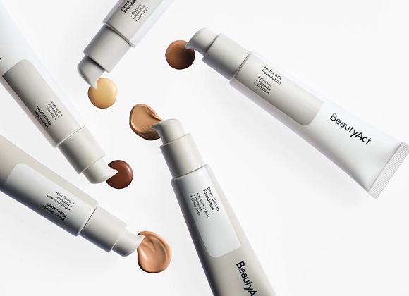 Kuva, joka näyttää erilaisia BeautyAct-meikkivoidetuotteita. Kuvassa näkyy viisi tuubia eri sävyillä meikkivoidetta, mukaan lukien vaalea, keskitumma ja tumma. Jokaisessa tuubissa on pumppu, joka vapauttaa pienen määrän meikkivoidetta. Tuotteet on aseteltu ympyrään valkoiselle taustalle.