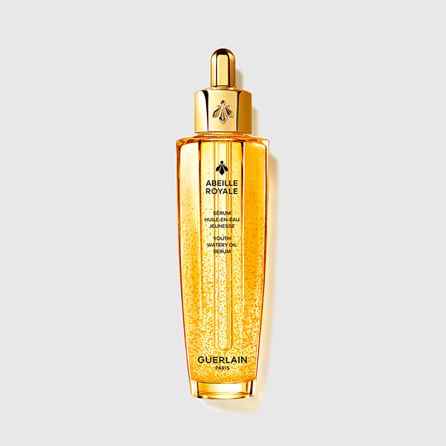 Guerlain Abeille Royale serum i en transparent gyllen flaske med pipette og synlige gyldne dråper. På flasken står “ABEILLE ROYALE”, “SERUM HUILE-EN-EAU JEUNESSE YOUTH WATERY OIL SERUM” og “GUERLAIN PARIS”.