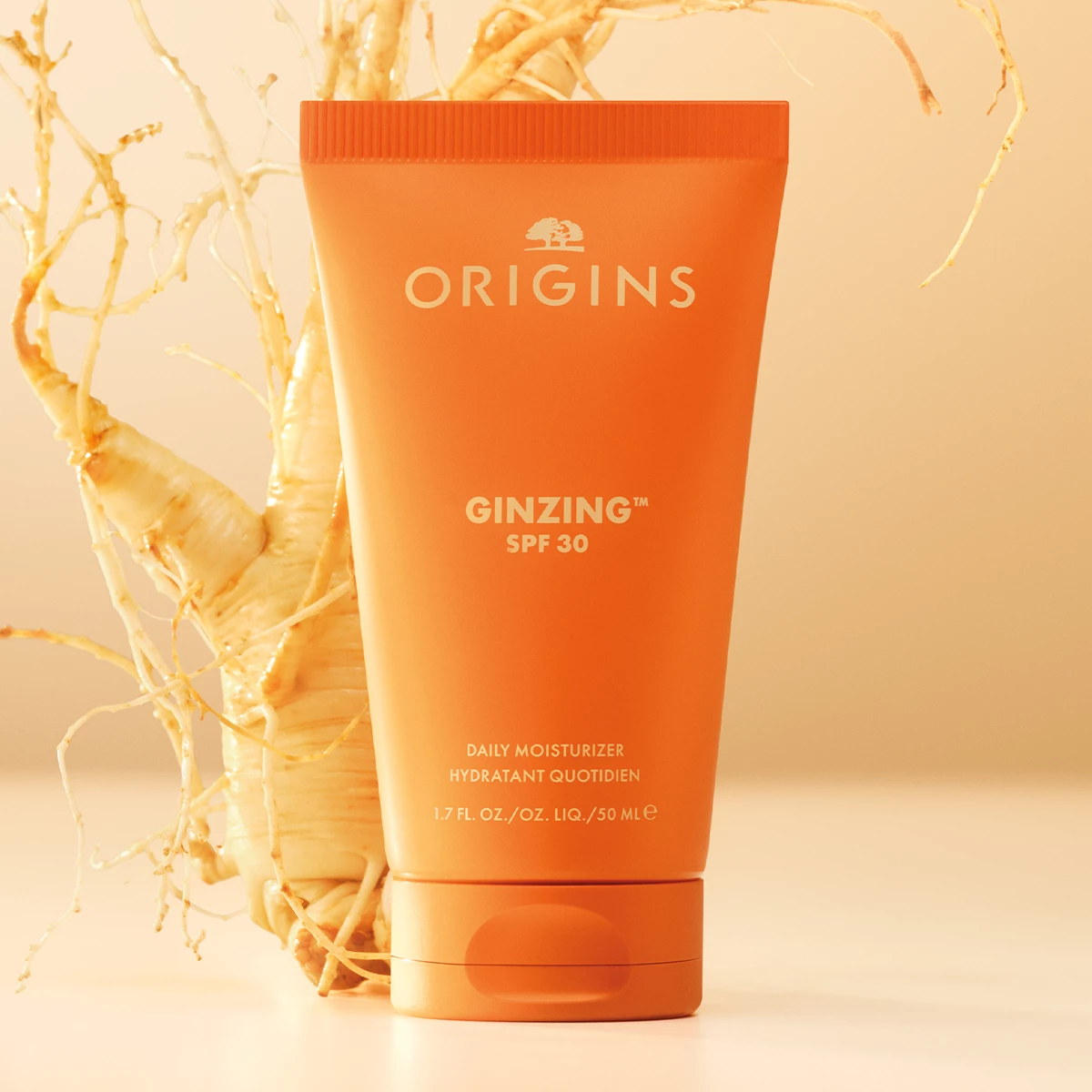 Origins GinZing SPF 30 Daily Moisturizer står foran en ginseng-rot mot en lysoransj bakgrunn.