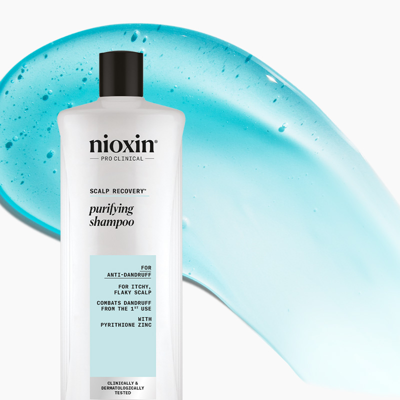 Nioxin Pro Clinical rensende sjampo mot flass i hvit flaske med svart hette, foran en blå bakgrunn.