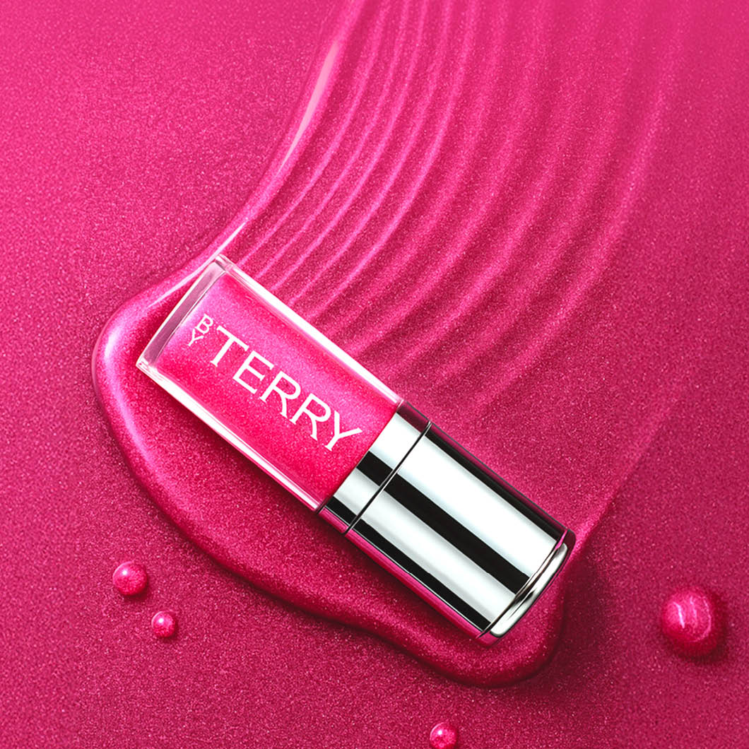 En ByTerry Baume lipgloss ligger mot en rosa lipgloss-bakgrunn.