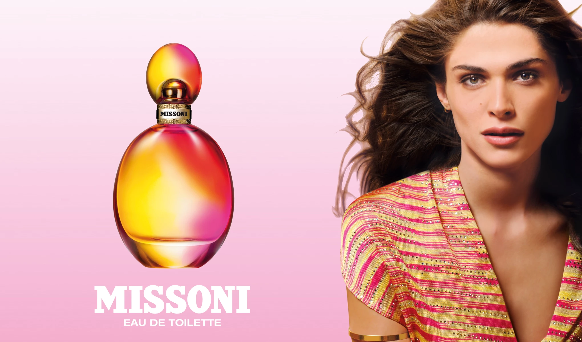 Missonin hajuvesipullo nimeltä ”Eau de Toilette”. Pullossa on värikäs muotoilu, jossa on vaaleanpunaisia, oransseja ja keltaisia elementtejä. Pullon oikealla puolella on nainen, jolla on pitkät kiharat hiukset ja jolla on yllään värikäs villapaita. Tausta on vaaleanpunainen, ja kuvassa on teksti ”Missoni Eau de Toilette”.