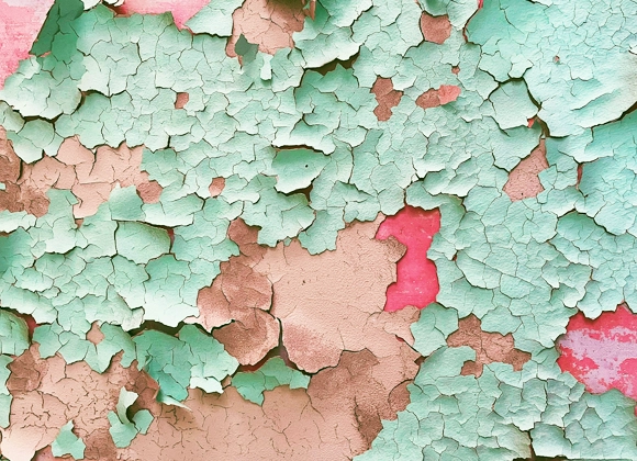 Närbild av en vägg med flagnande färg i turkosa, rosa och beige nyanser som avslöjar flera lager underliggande färg.