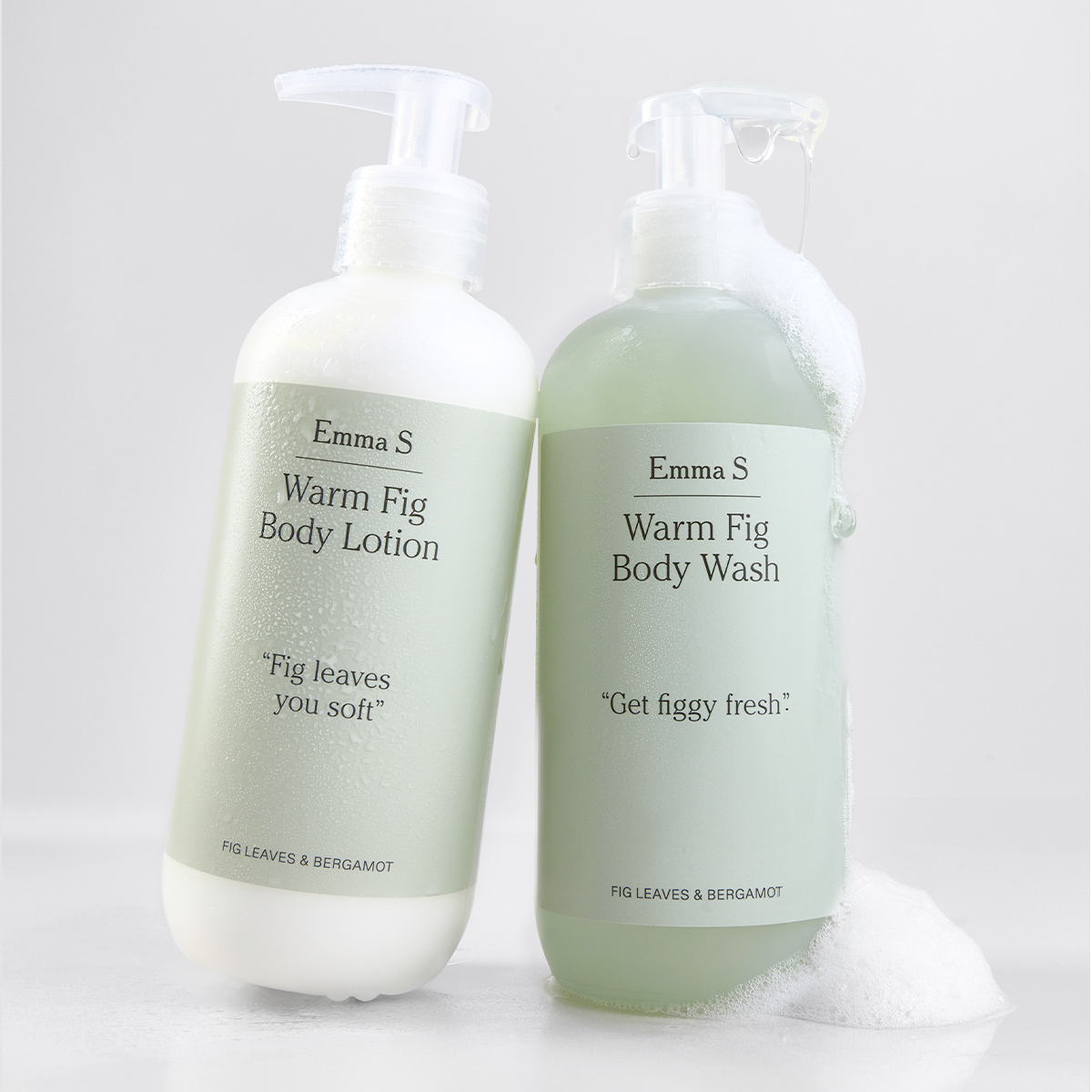 Två pumpflaskor från Emma S med kroppsvård, “Warm Fig Body Lotion” och “Warm Fig Body Wash”, med texterna “Fig leaves you soft”, “Get figgy fresh” och “Fig Leaves & Bergamot”, en med synligt skum på en ljus bakgrund.