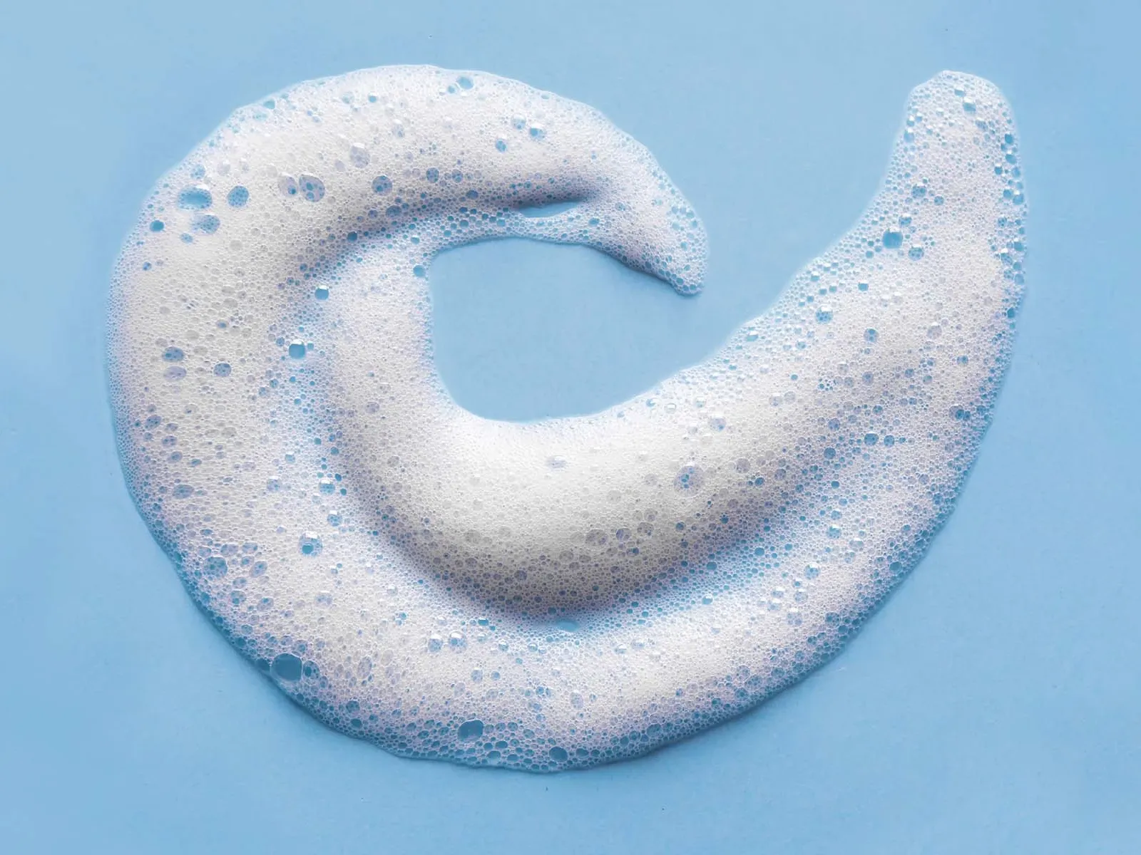 Vitt skum med bubblor format som en spiral, mot ett blått underlag.
