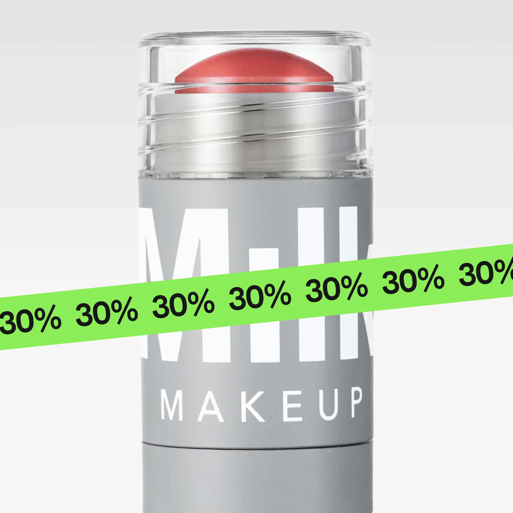 Milk Makeup-stick i lys grå emballasje med korallfarget produkt vises mot lys grå bakgrunn. En grønn banner med gjentatt tekst «30%» dekker nedre del av bildet, og emballasjen viser teksten MILK MAKEUP.