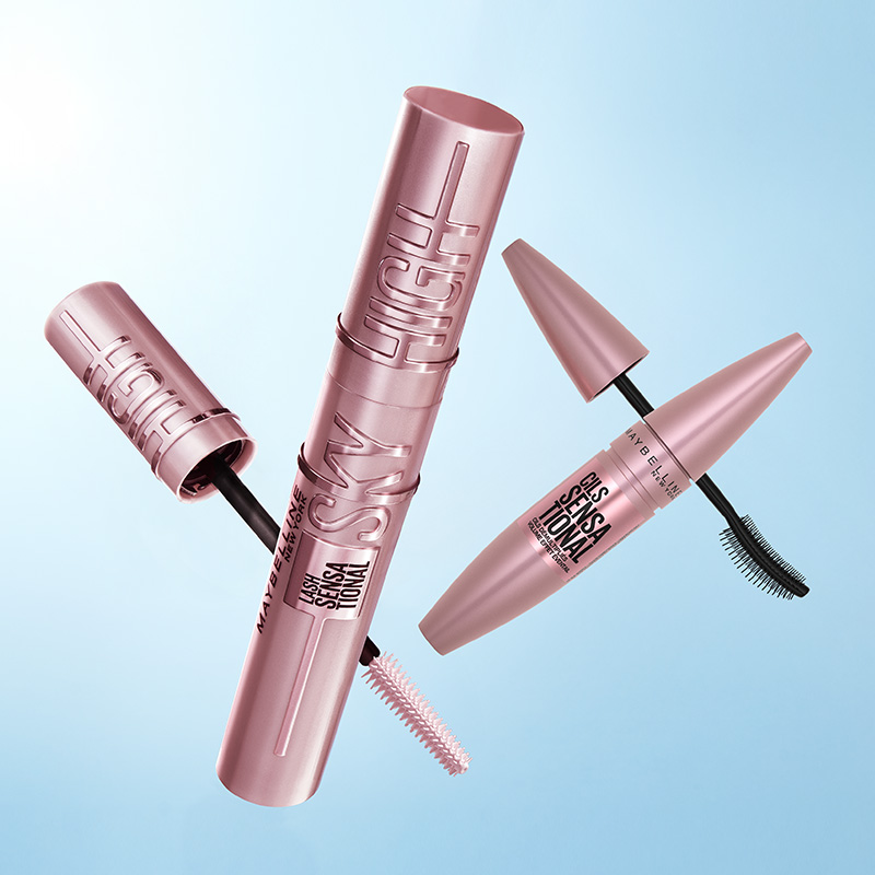 Maybelline-mascaror i rosa förpackningar mot blå bakgrund, med synliga borstar.