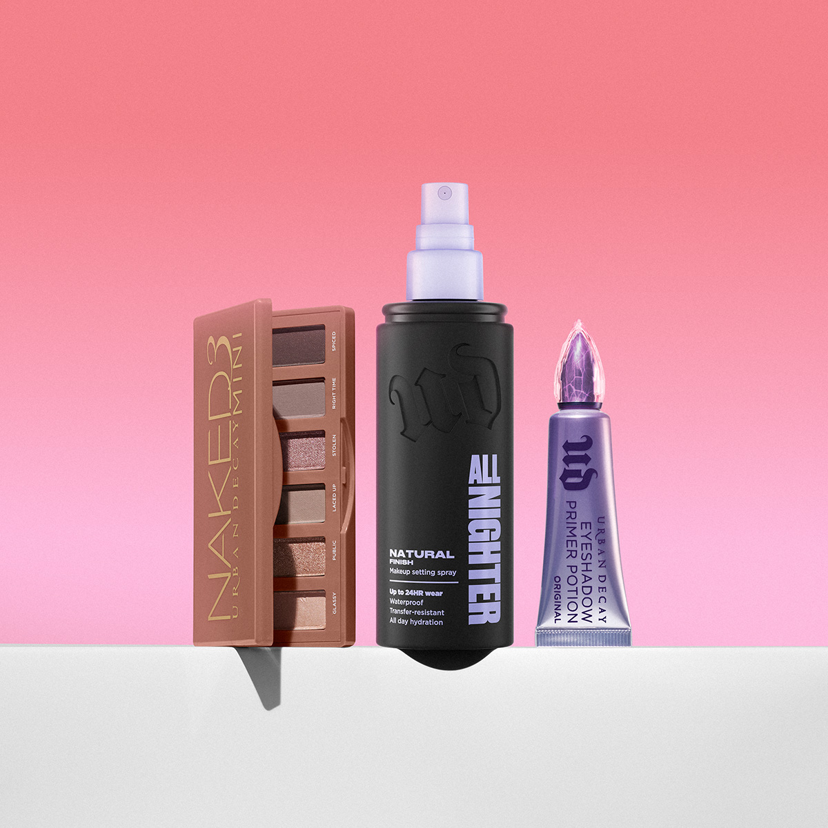 Urban Decay Naked3-øyenskyggepalett, All Nighter-settingspray og Eyeshadow Primer Potion mot rosa bakgrunn.