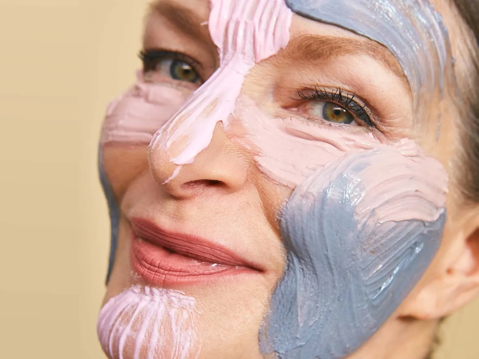 Närbild av kvinna med mogen hud som applicerat färgglada ansiktsmasker i olika zoner i ansiktet