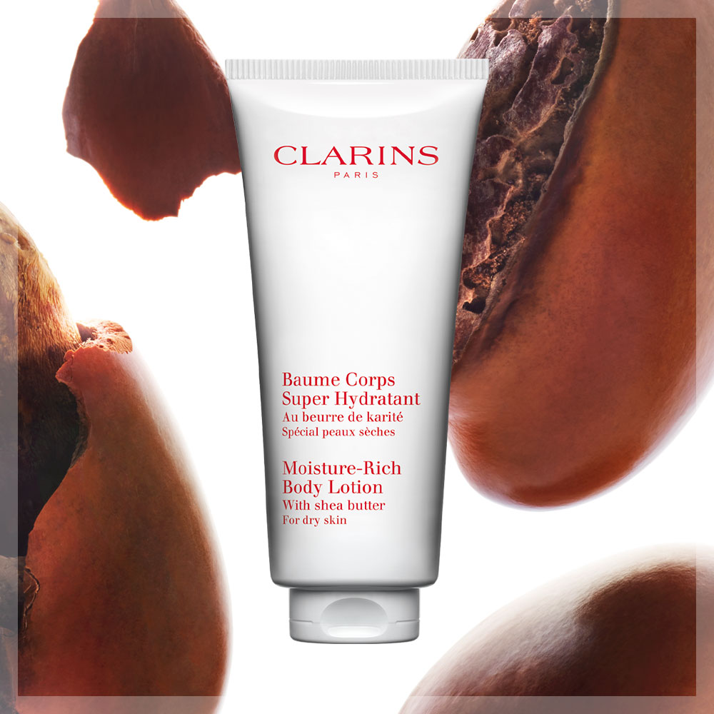 Clarins produkt «Baume Corps Super Hydratant», mot en bakgrunn av sheanøtter. Teksten på produktet er både på fransk og engelsk og beskriver det som en fuktighetsgivende bodylotion for tørr hud.