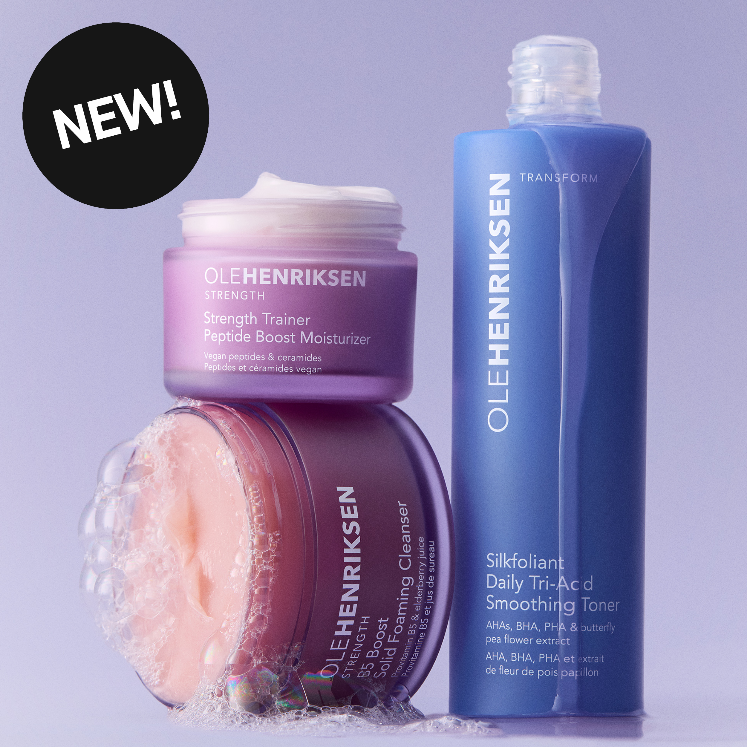 OLEHENRIKSEN Strength Trainer Peptide Boost Moisturizer, Truth Juice Daily Cleanser och Transform Silkfoliant Daily Tri-Acid Smoothing Toner visas mot en ljuslila bakgrund. En svart cirkel med texten ”NEW” syns tillsammans med produktnamn och ingredienstext som ”AHAs, BHA, PHA & butterfly pea flower extract”.