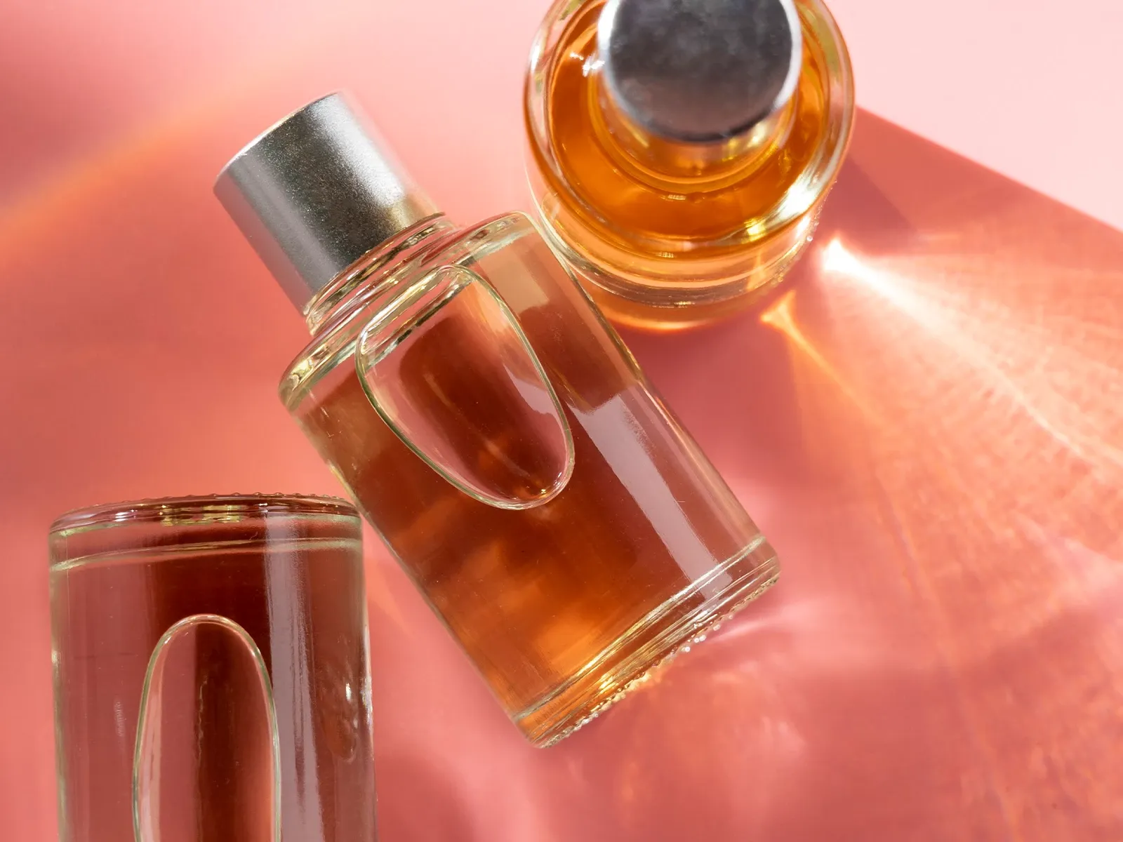 Tre parfymeflasker med oransje væske på en rosa bakgrunn.