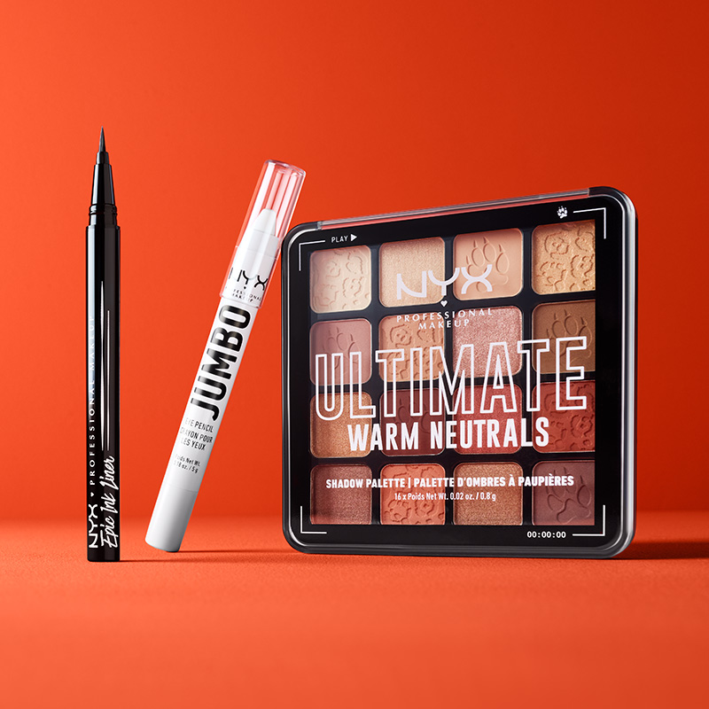 Tre NYX Professional-Makeup-produkter mot en rød bakgrunn. Produktene inkluderer en svart eyelinerblyant, en hvit øyeblyant og en øyenskyggepalett.
