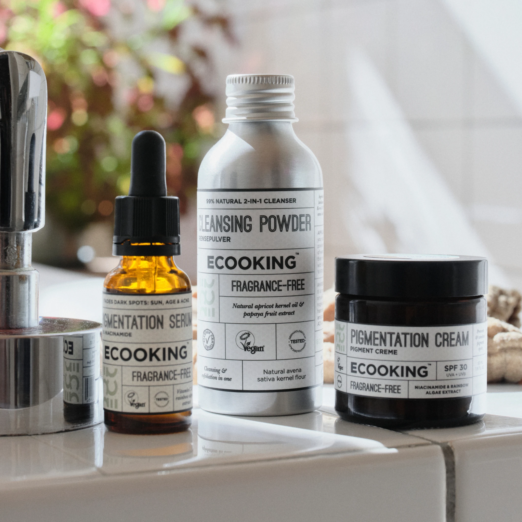 Ecooking hudpleieprodukter plassert ved en servant med uskarp bakgrunn. På emballasjen vises blant annet tekstene «PIGMENTATION SERUM», «CLEANSING POWDER», «PIGMENTATION CREAM», «ECOOKING» og «FRAGRANCE-FREE».