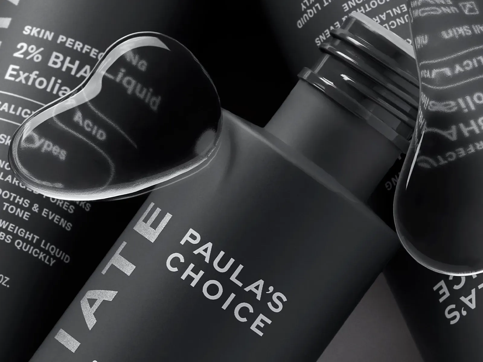 Tre produkter fra Paula's Choice i nærbilde med grå bakgrunn og vanndråper i forgrunnen.