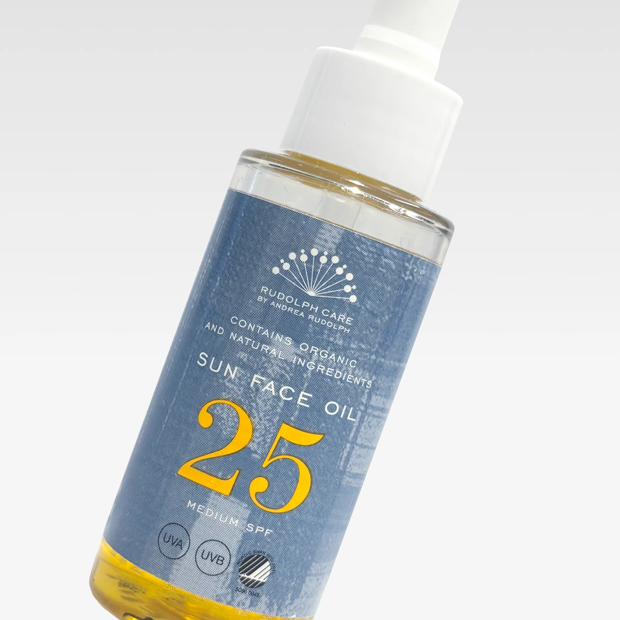Rudolph Care Sun Face Oil 25 SPF i flaska med pipett mot ljusgrå bakgrund. På etiketten syns texterna ”RUDOLPH CARE BY ANDREA RUDOLPH”, ”CONTAINS ORGANIC AND NATURAL INGREDIENTS”, ”SUN FACE OIL”, ”25”, ”MEDIUM SPF”, ”UVA” och ”UVB”.