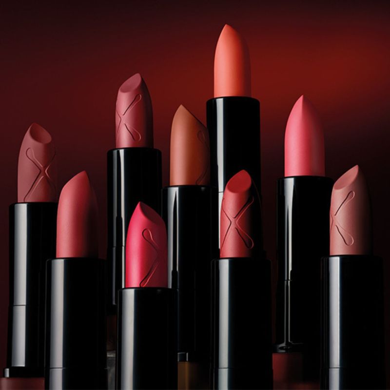 Flera läppstift från Max Factor i olika nyanser av rött, rosa och brunt, placerade mot en mörkröd bakgrund.