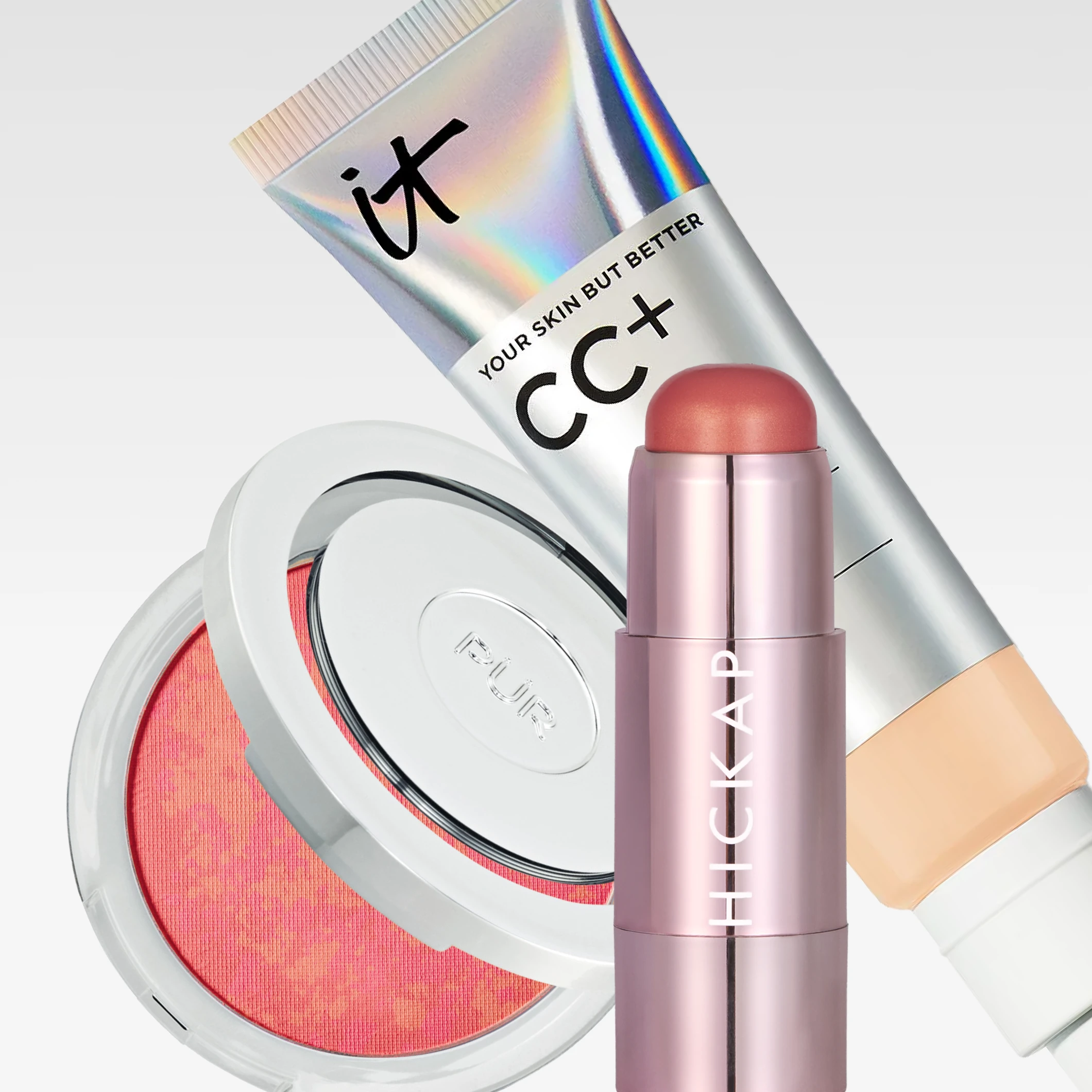 Tre makeup-produkter mot lys grå bakgrunn: IT Cosmetics CC+ Color-Correcting Full-Coverage Cream SPF 50+, PÜR pudderrouge i åpen kompakt og HICKAP makeupstick. Synlig tekst inkluderer «it», «YOUR SKIN BUT BETTER», «CC+», «COLOR-CORRECTING», «Full-Coverage Cream», «Hydrating Serum», «SPF/FPS UVB 50+», «PÜR» og «HICKAP».