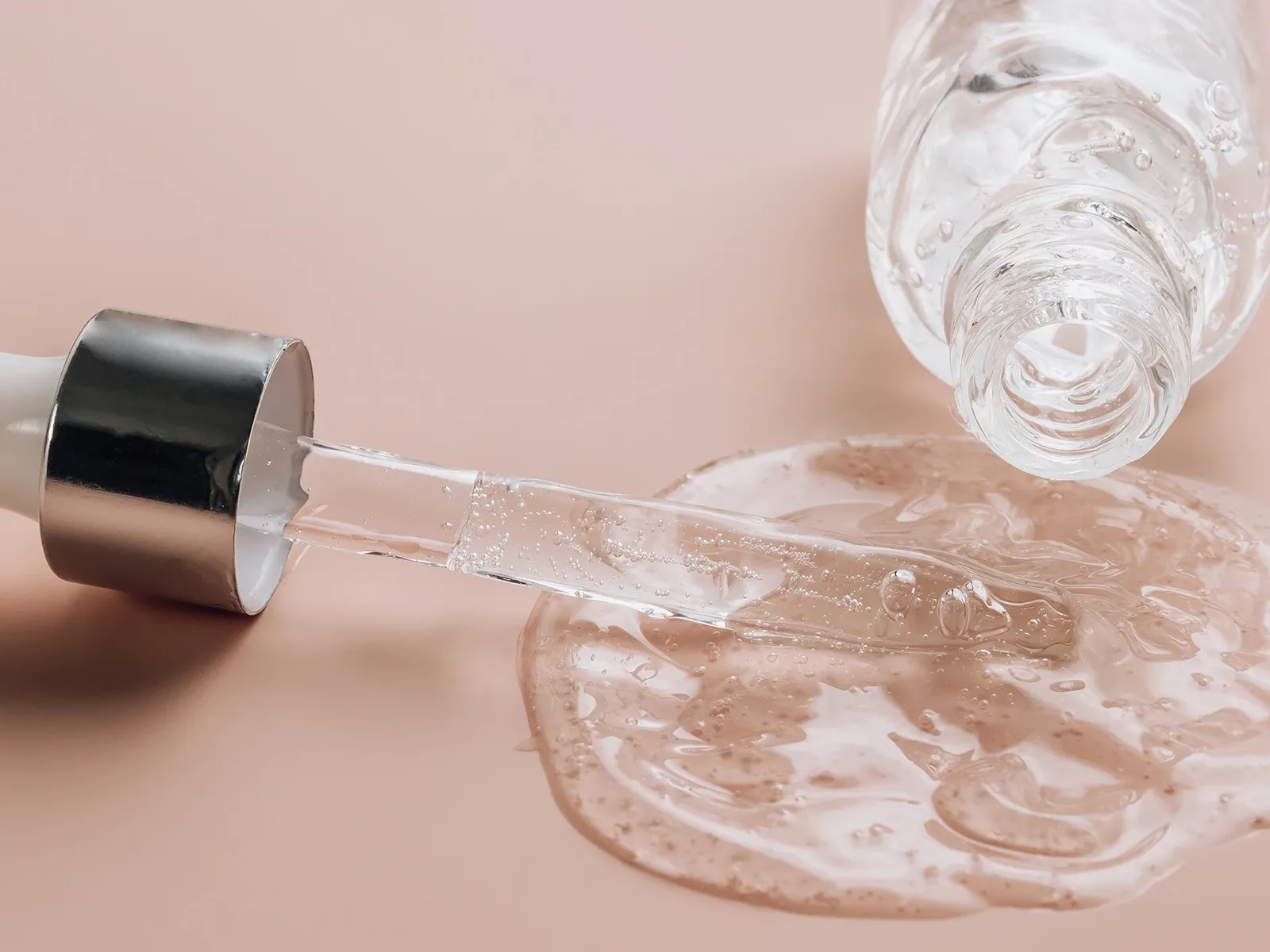 En pipette og en flaske med gjennomsiktig væske som har sølt ut på en beige overflate.