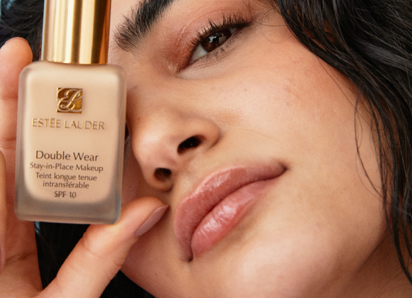 En hand håller en flaska Estée Lauder Double Wear Stay-in-Place Makeup SPF 10. Flaskan har en guldlock och texten på flaskan är tydligt synlig
