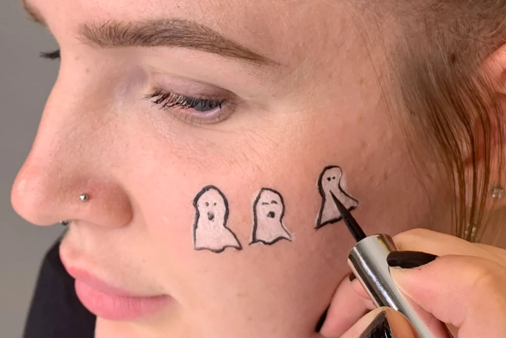 Henkilö piirtää kasvot valkoiseen aaveen muotoon poskelleen mustalla nestemäisellä eyeliner-kynällä.