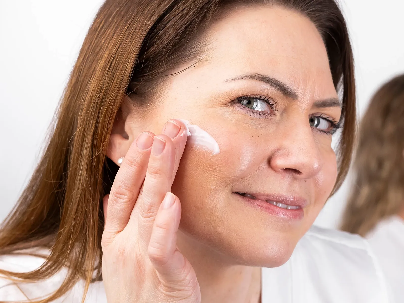 En person med langt brunt hår som påfører hudkrem på kinnet.