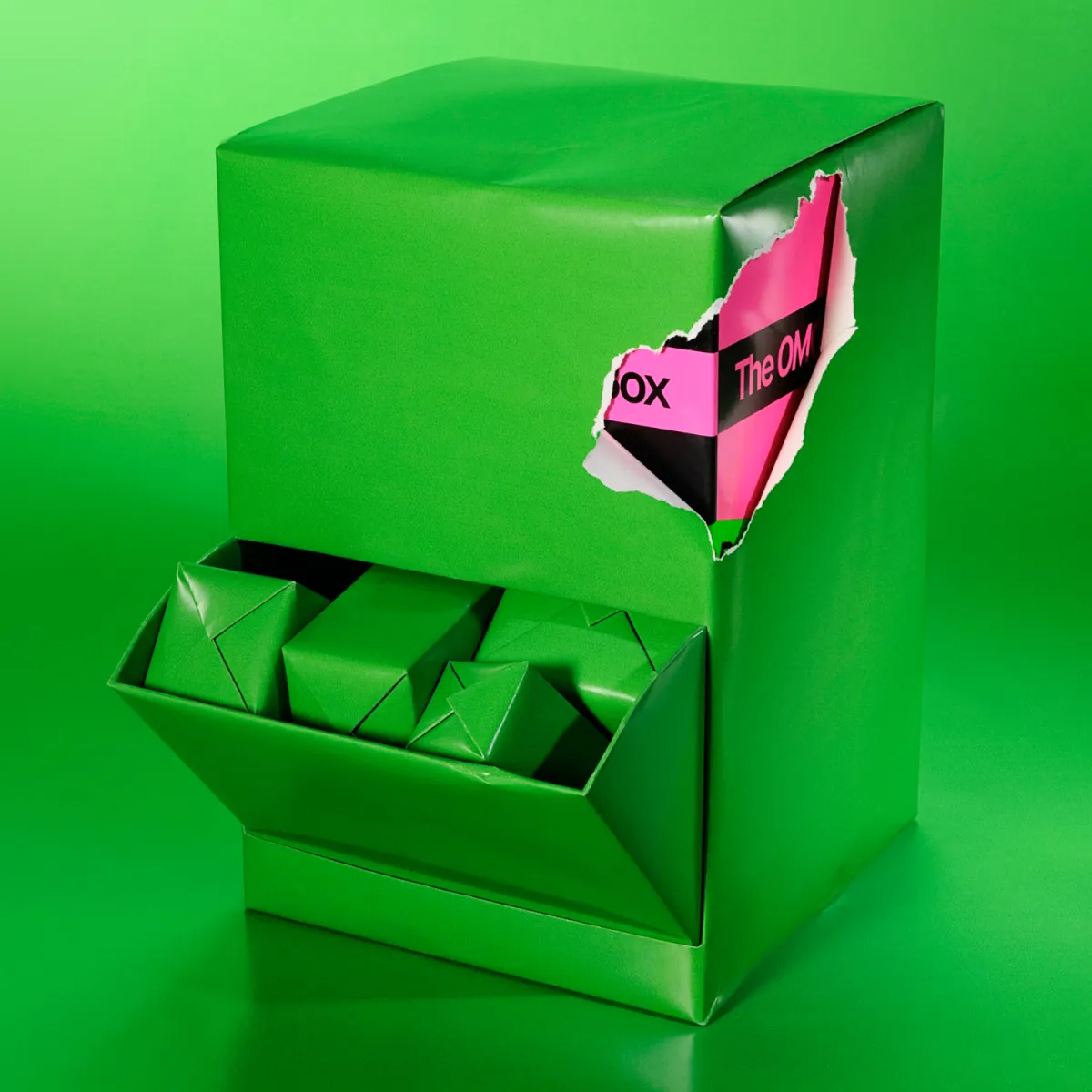 Vihreään paperiin kääritty laatikko vihreällä taustalla. Avoimessa lokerossa on pieniä vihreitä paketteja, ja repeytyneestä kohdasta pilkistää pinkki ja musta pakkaus.