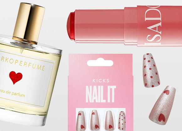 Ett urval skönhetsprodukter mot ljus bakgrund. En parfymflaska med guldfärgad kork och etikett med rött hjärta, ett rosa läppstift med texten “ISAD”, ett rosa förpackningskort märkt “KICKS NAILIT” samt lösnaglar i ljusrosa nyanser med hjärt- och prickmönster.