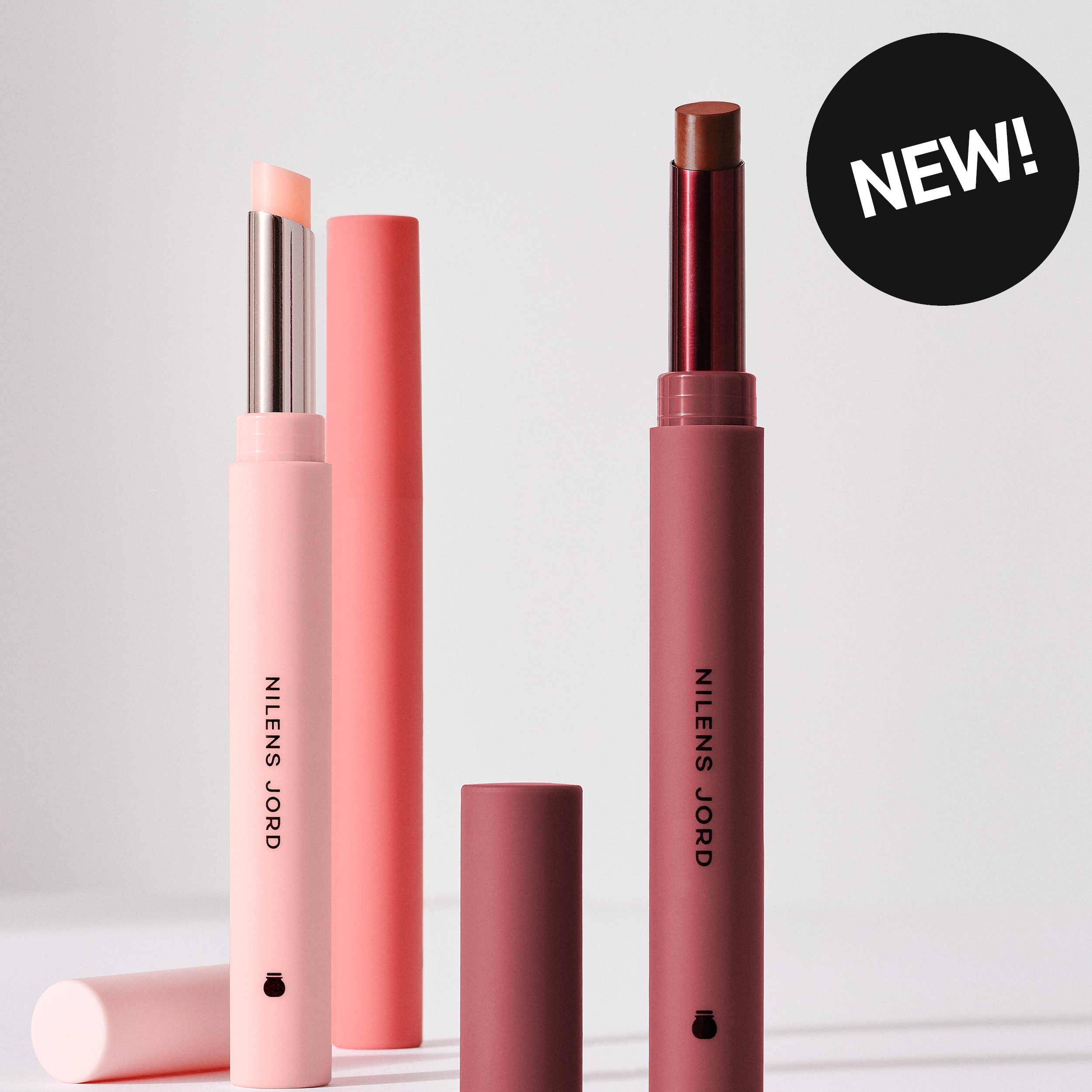 To leppeprodukter fra Nilens Jord i rosa og brun nyanse med synlige stifter og emballasje merket “NILENS JORD”, samt en svart sirkel med teksten “NEW!”.