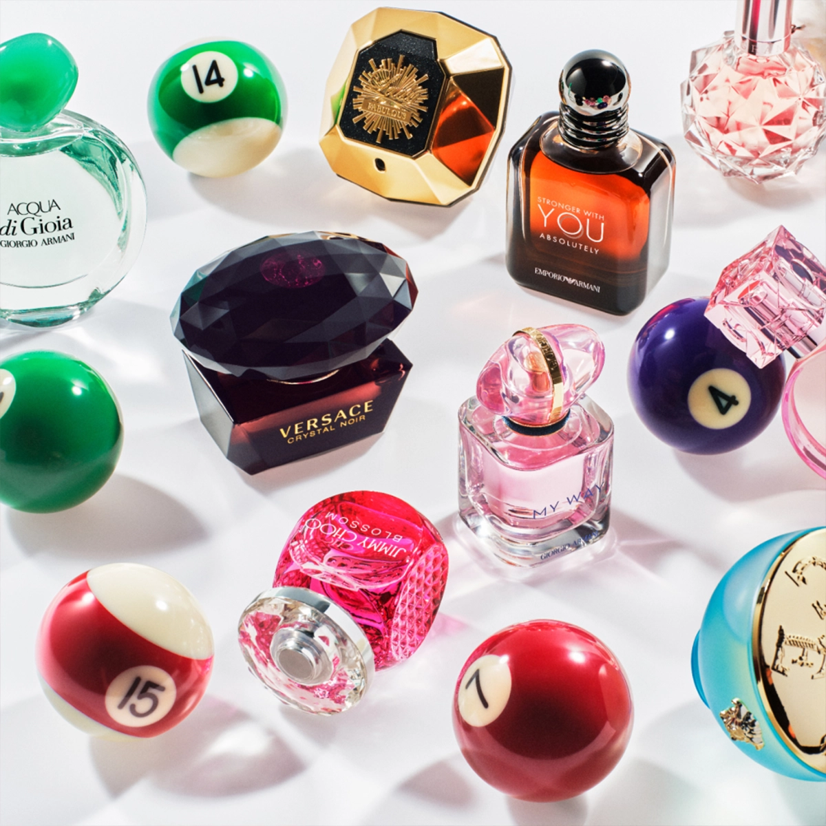 Bild som visar flera parfymflaskor arrangerade bland biljardbollar. Parfymerna inkluderar Acqua di Gioia från Giorgio Armani, Versace Crystal Noir, Stronger With You Intensely från Emporio Armani, My Way från Giorgio Armani, och andra. Bakgrunden är vit.