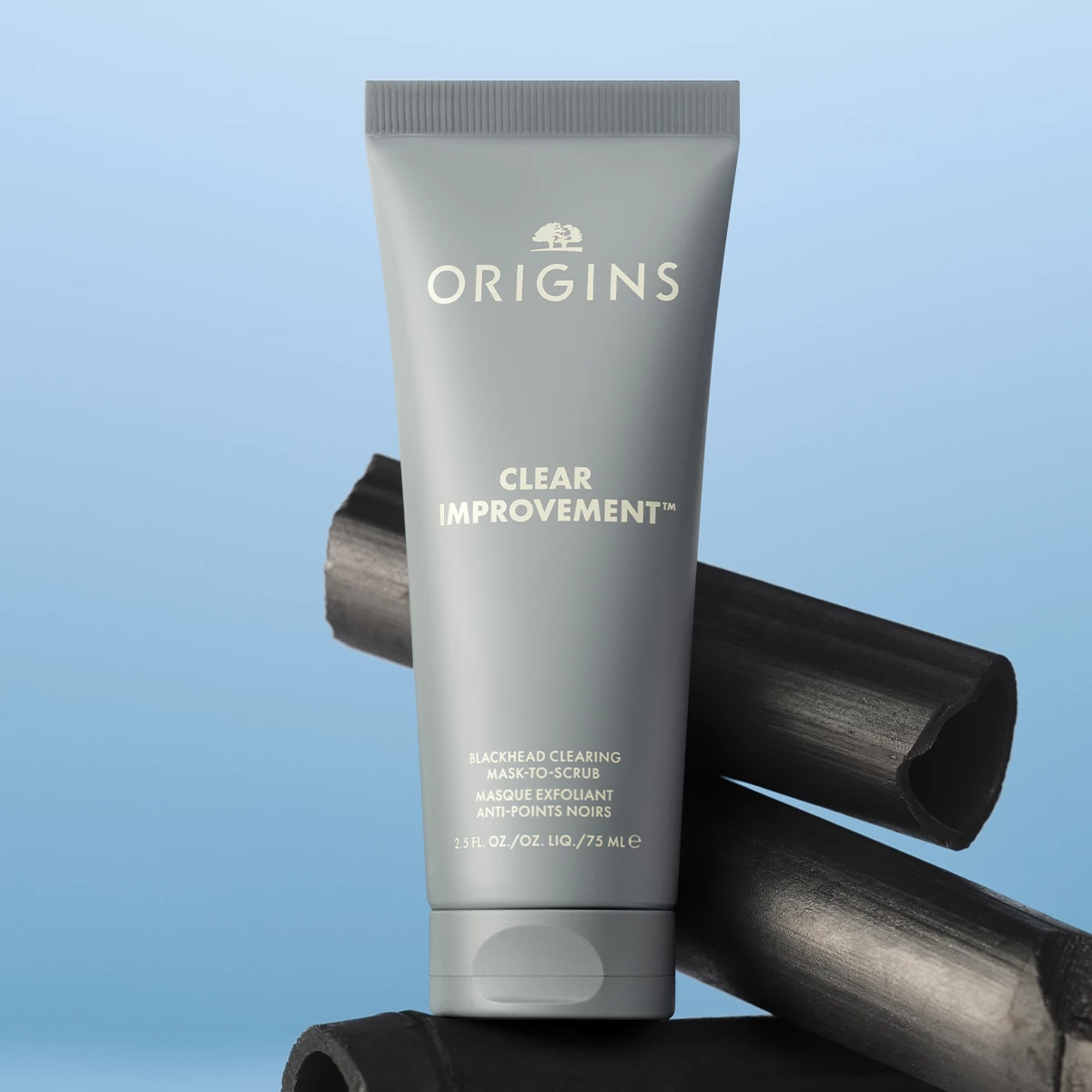 Origins Clear Improvement Blackhead Clearing Mask-to-Scrub plassert foran biter av aktivt kull mot en lys blå bakgrunn.