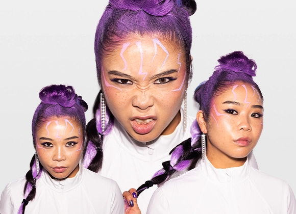 Bilden visar samma person tre gånger med lila hår i olika poser och vinklar. Personen bär en vit topp och har lila naglar. Personen står mot en vit bakgrund.