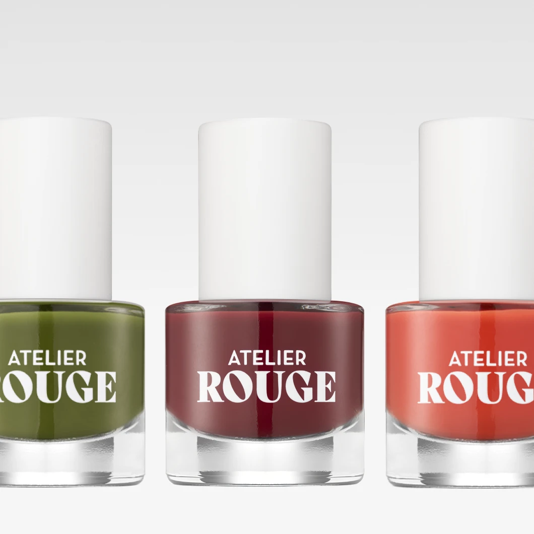 Bilde som viser tre neglelakkflasker fra Atelier Rouge. Fargene på neglelakken er grønn, vinrød og oransje. Bakgrunnen er hvit.