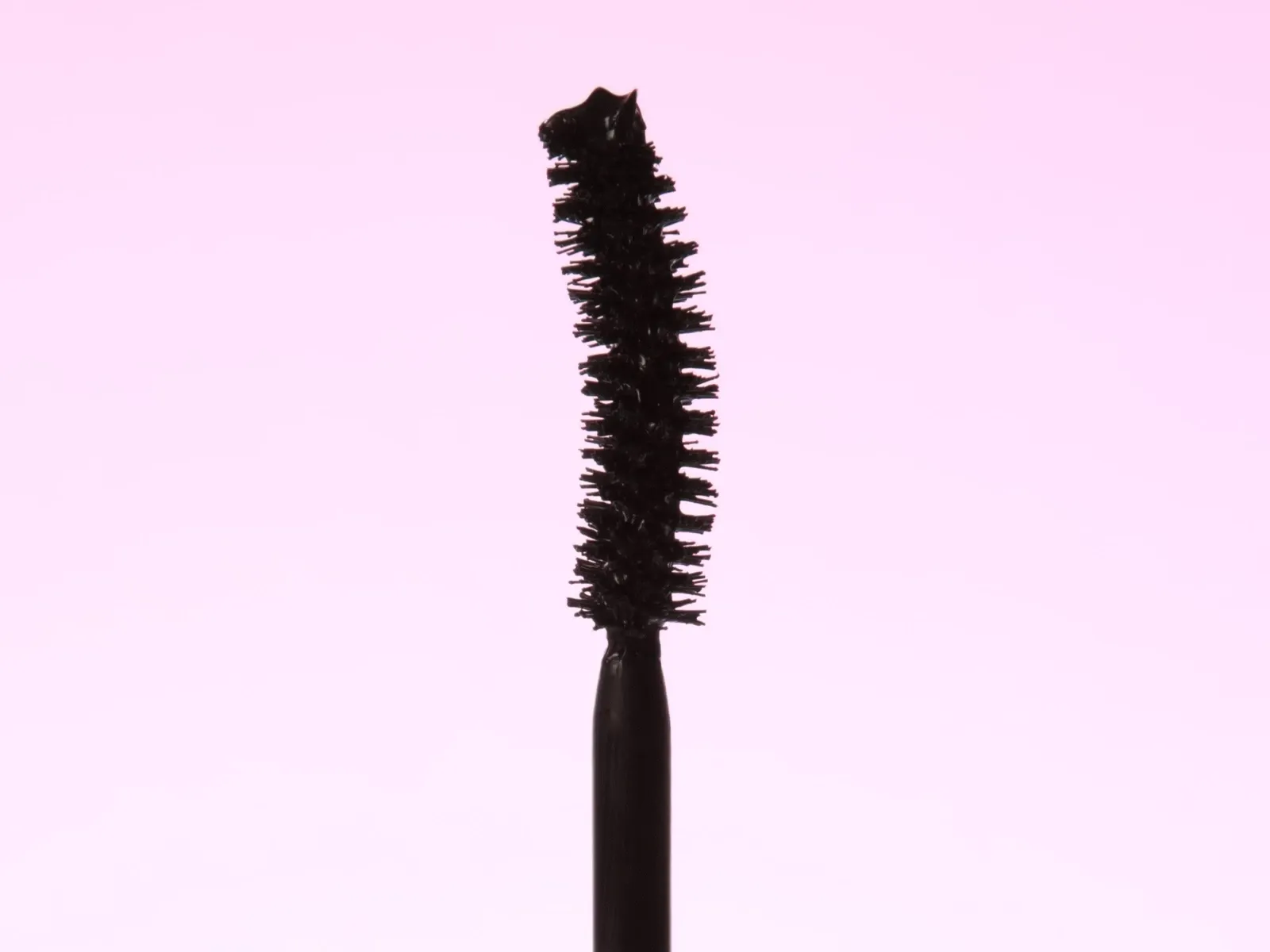 Et nærbilde av en mascarabørste med svart mascara mot en rosa bakgrunn.