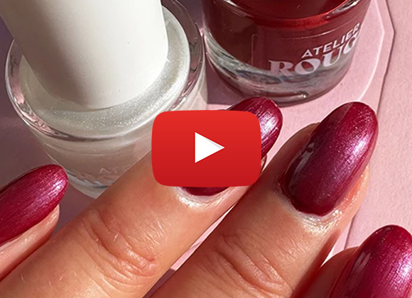 Närbild på en hand med rödmålade naglar som håller i två nagellacksflaskor, en vit och en röd. En YouTube-symbol är synlig på bilden.