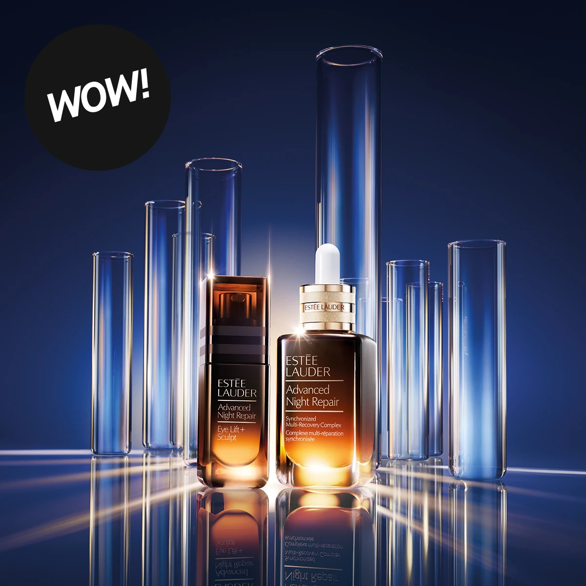 Estée Lauder Advanced Night Repair Eye Lift + Sculpt och Advanced Night Repair Synchronised Multi-Recovery Complex serum står framför höga glasrör mot en mörkblå bakgrund. Texten "WOW!" visas i en svart cirkel i bildens övre vänstra hörn.