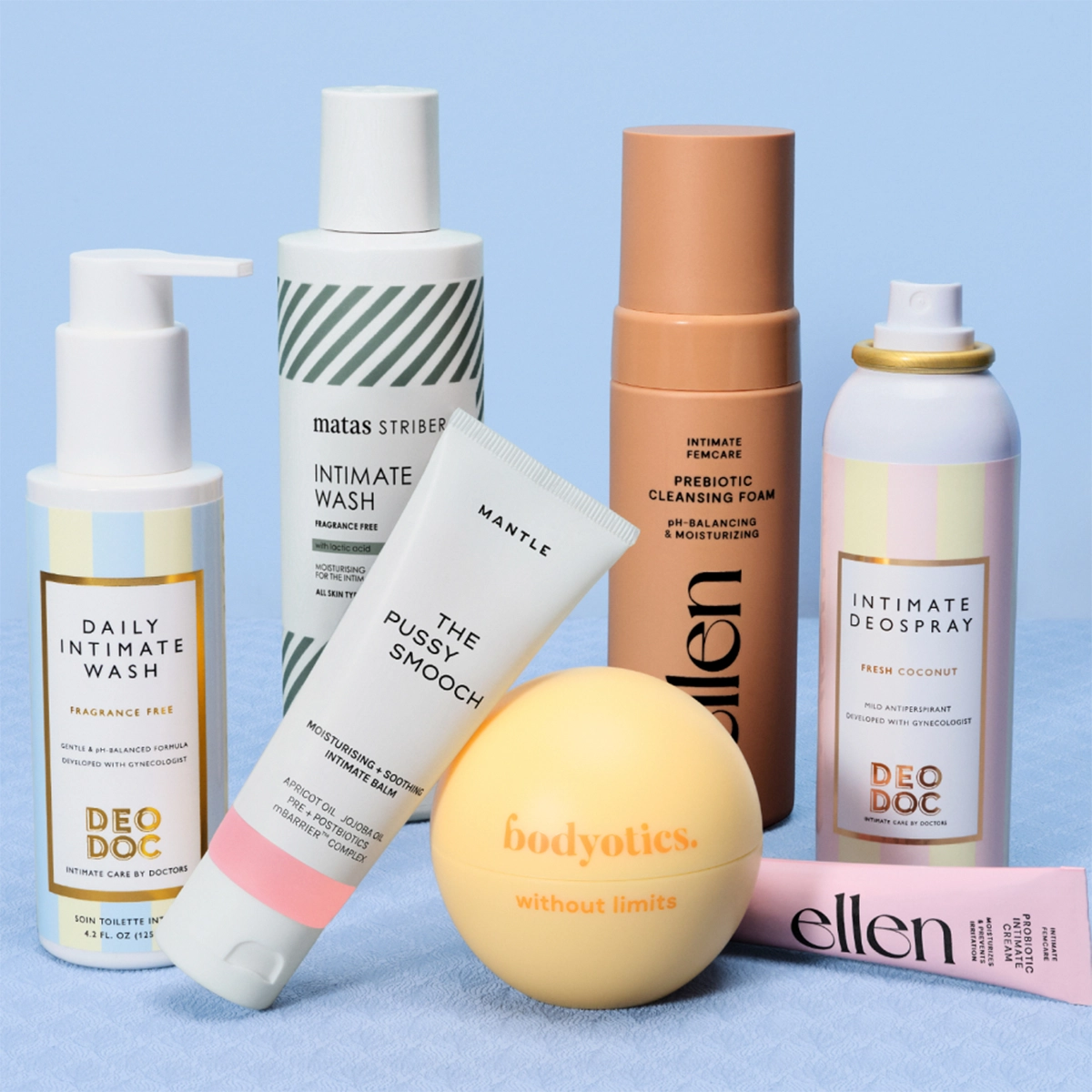 Flere intimpleie- og hudpleieprodukter står oppstilt mot en lys blå bakgrunn, blant annet DeoDoc Daily Intimate Wash Fragrance Free, Matas Striber Intimate Wash, Mantle The Pussy Smooch, ellen Prebiotic Cleansing Foam, Bodyotics without limits og Intimate Deospray Fresh Coconut. Produktene vises i pastellfarget emballasje med synlige merkenavn og tekst for intimvask, prebiotisk rens, deodorantspray og fuktgivende intimpleie.