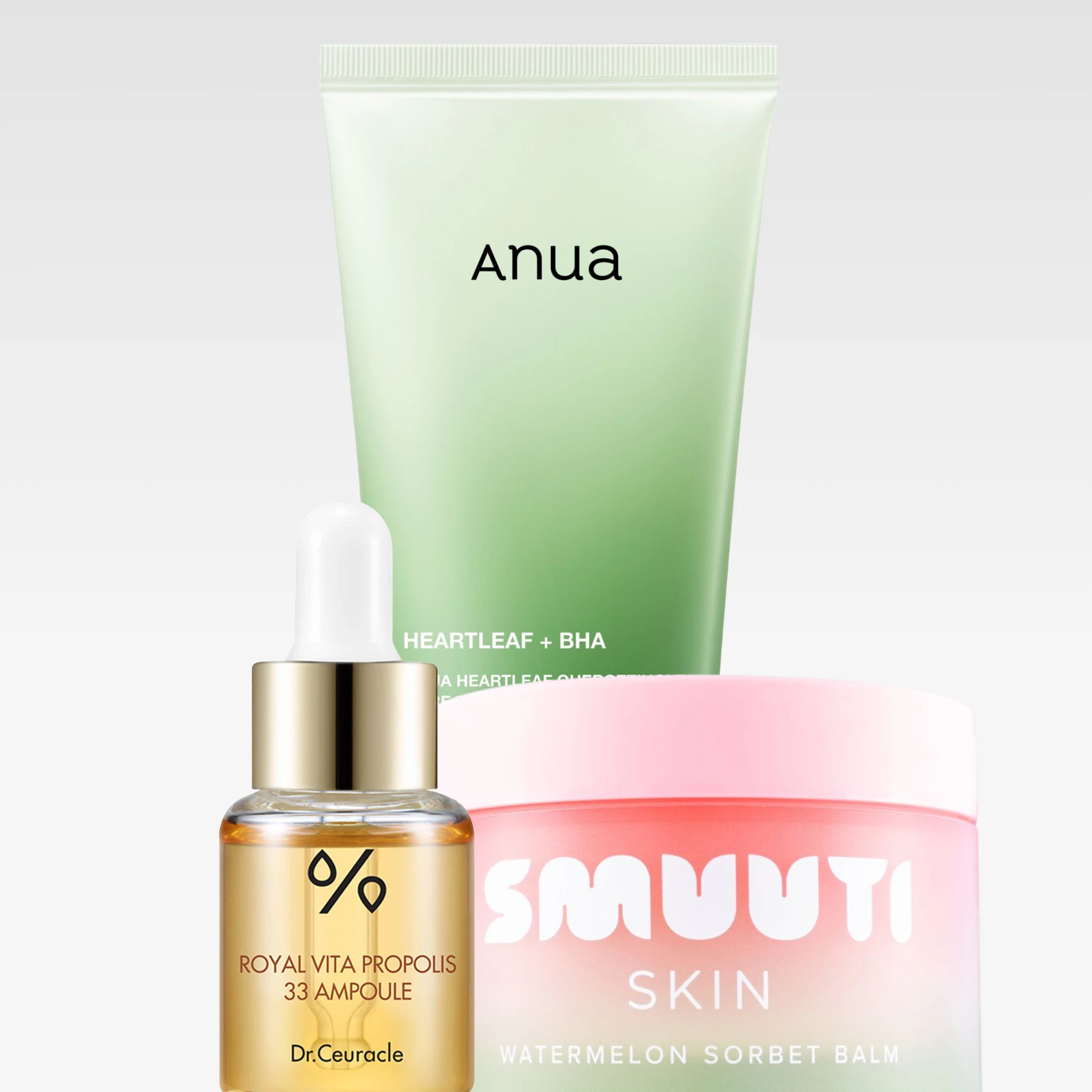 Produktbild med tre K-beauty hudvårdsprodukter mot ljus bakgrund: en grön tub märkt ”Anua Heartleaf + BHA”, en rosa burk märkt ”Smuuti Skin Watermelon Sorbet Balm” samt en glasflaska med pipett märkt ”Dr. Ceuracle Royal Vita Propolis 33 Ampoule”.