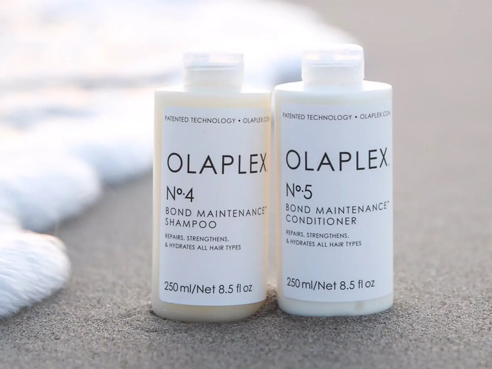 Två produkter av olaplex placerade på en strand intill vatten