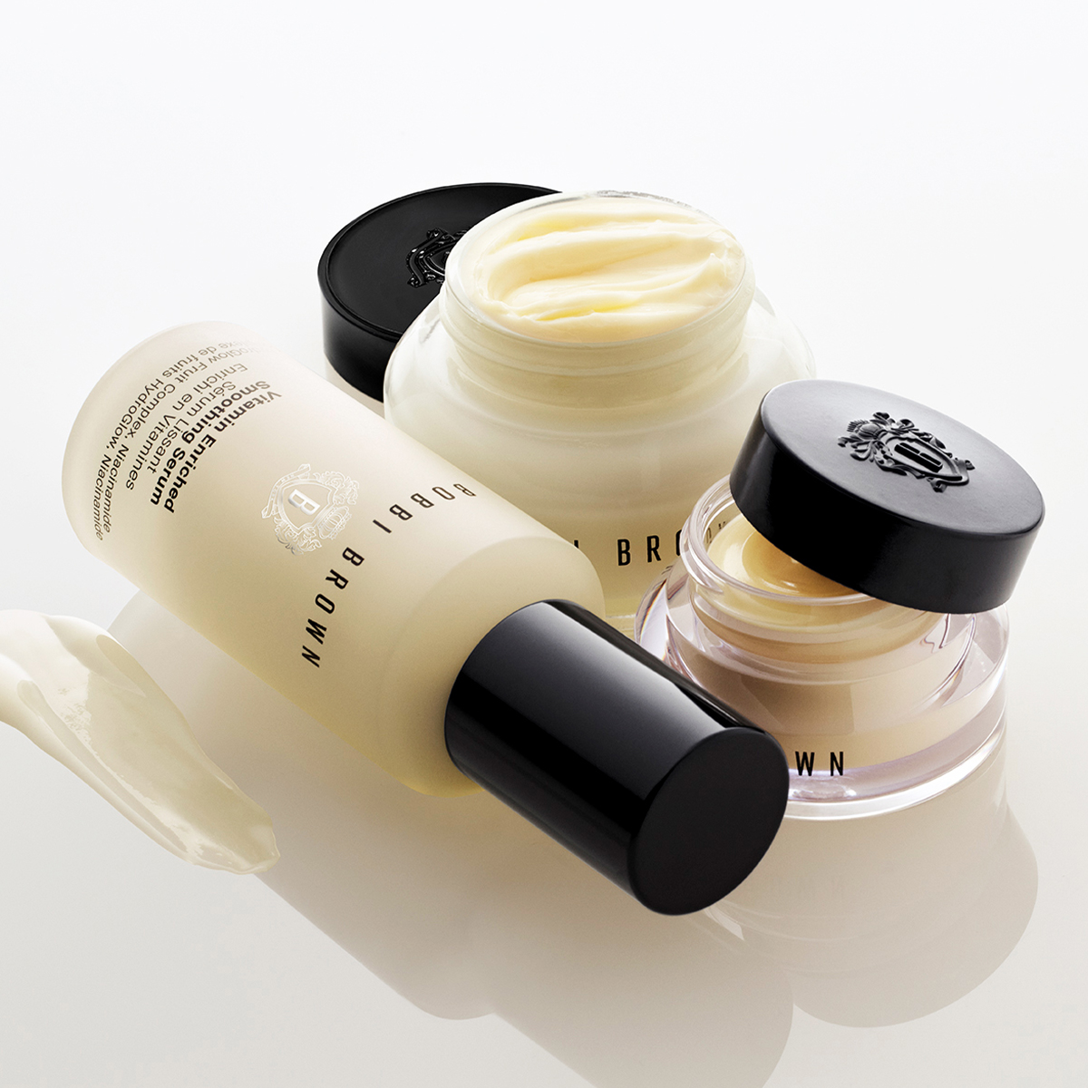 Bobbi Brown Vitamin Enriched Face Base, Vitamin Enriched Smoothing Serum ja Vitamin Enriched Eye Base on esitelty yhdessä vaaleaa taustaa vasten. Kuvassa näkyy avoin kasvovoide, avoin silmänympärysvoide, seerumi mustalla pumppupullolla sekä voidelevitys. Näkyvä teksti: "BOBBI BROWN", "Vitamin Enriched Smoothing Serum", "Face Oil + Vitamin C Complex + Vitamin E", "96% of Fruits" ja "Vitamin Enriched Eye Base".