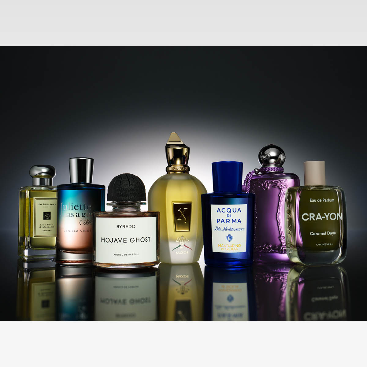 Rivissä ylellisiä niche-hajuvesipulloja eri väreissä ja muodoissa, aseteltuna tummalle, kiiltävälle pinnalle. Kokonaisuus viestii eksklusiivisuutta ja monipuolisia tuoksuelämyksiä.