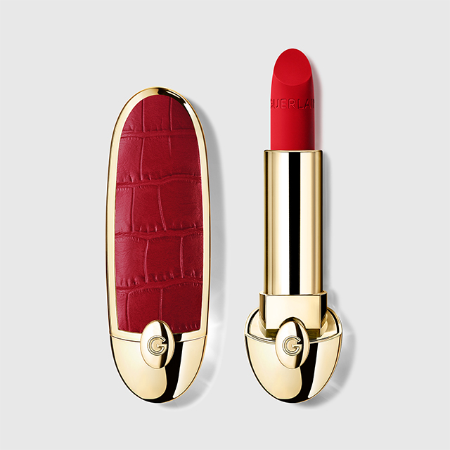 Rød leppestift fra Guerlain med gullfarget hylse og rød, mønstret kork med “G”-logo. Leppestiften er skrudd opp og viser en intens rød nyanse med teksten “GUERLAIN” preget på produktet.